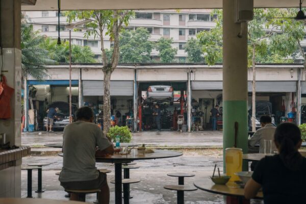 View from an open-sided hawker centre towards neighbouring motor-repair bays at Alexandra Village