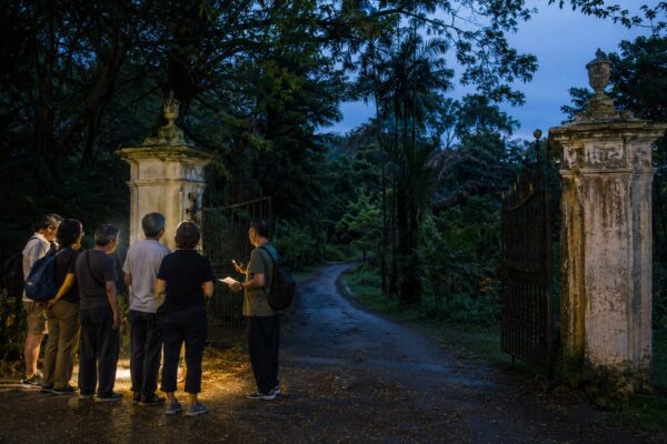 A small organised heritage group gathering at cemetery gates at blue hour