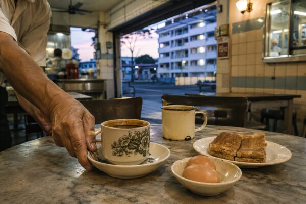 A worker setting a porcelain kopi cup and saucer on a marble-topped table at dawn
